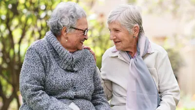 Deux dames âgées souriantes sur un banc en train de se parler