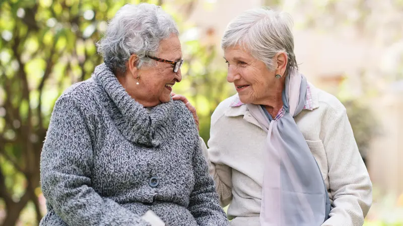 Deux dames âgées souriantes sur un banc en train de se parler